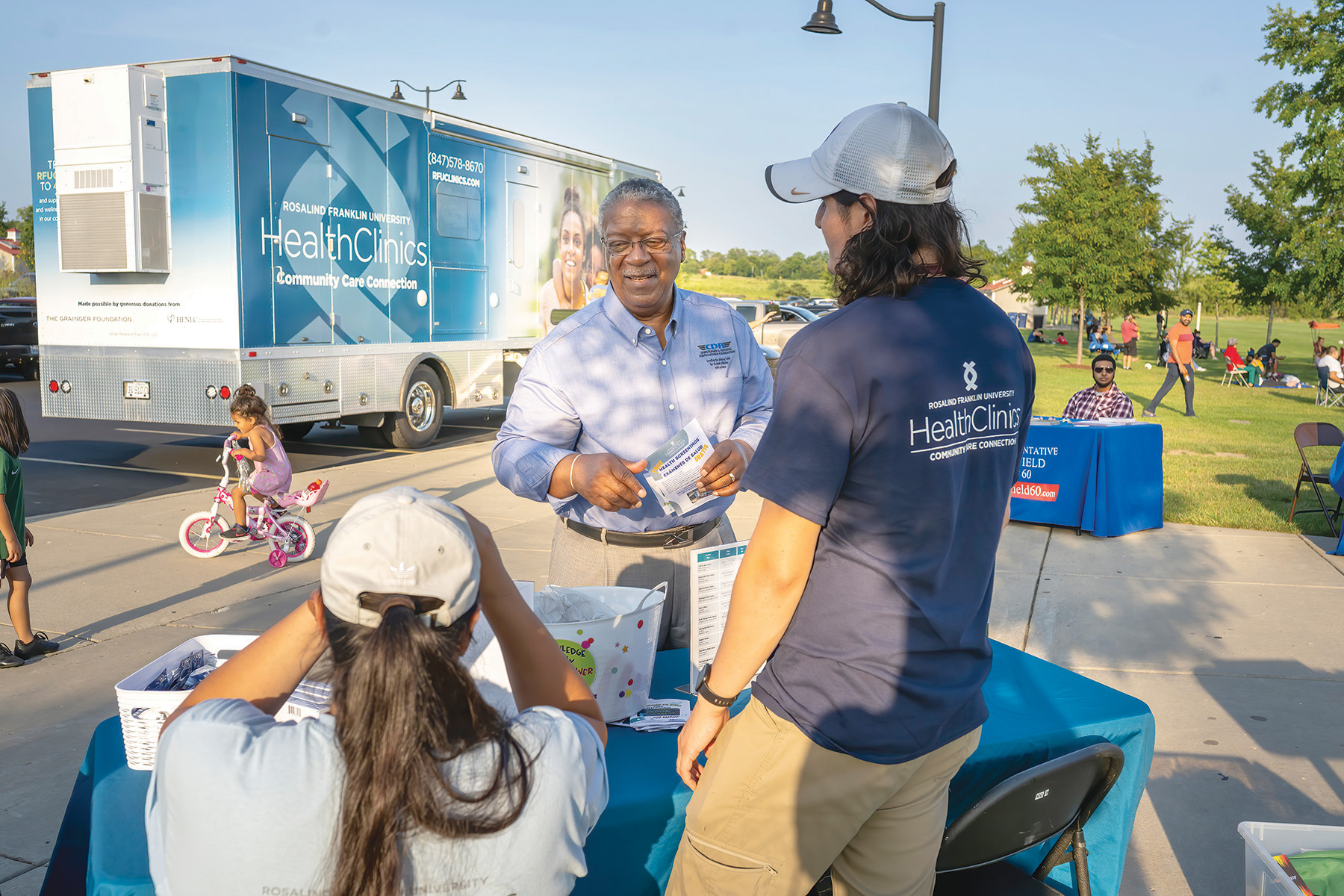 A community member talks with members of the Community Care Coach staff, with the mobile care clinic in the background.